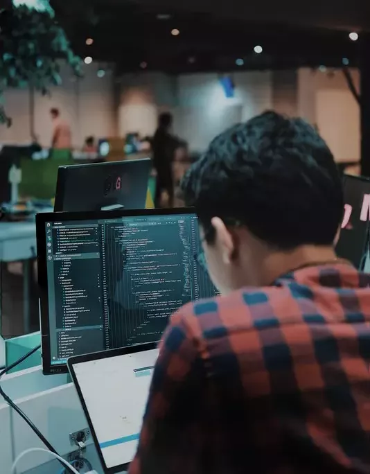 Student coding on dual screens in a collaborative workspace, learning via Sigma School's free Coding Fundamentals for beginners