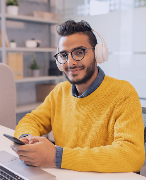 A man in headphone and glasses smiling at the camera, representing a friendly and approachable team member ready to assist you with your learning journey at Sigma School